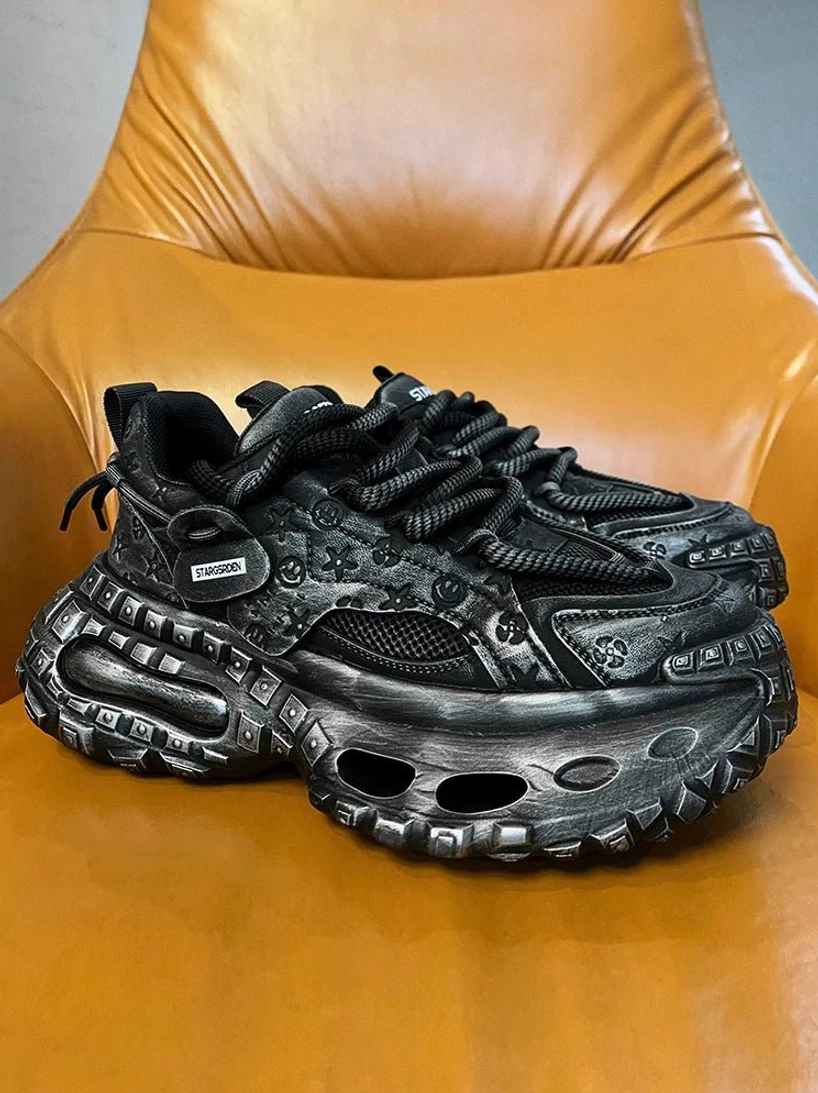 Pair of black chunky platform sneakers in a side three-quarter view featuring hollowed rubber soles, mesh side panels, and embossed decorative textures
