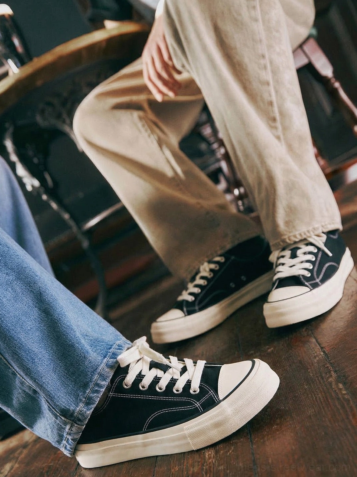 Black and white low-top vulcanized platform canvas sneakers styled with denim and khaki trousers indoors