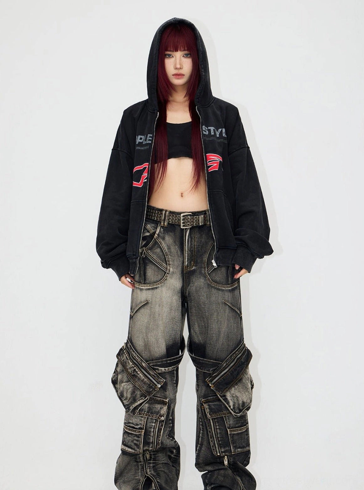 Cropped styling view of a black washed distressed hooded jacket worn over a fitted top with cargo jeans for an urban streetwear outfit