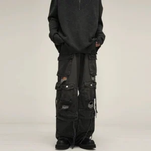 Black washed distressed wide-leg cargo jeans front view featuring layered flap pockets, ripped cutout details, baggy denim fit, and drawstring cuffs
