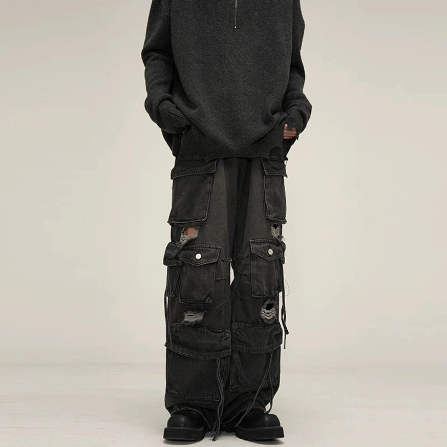 Black washed distressed wide-leg cargo jeans front view featuring layered flap pockets, ripped cutout details, baggy denim fit, and drawstring cuffs