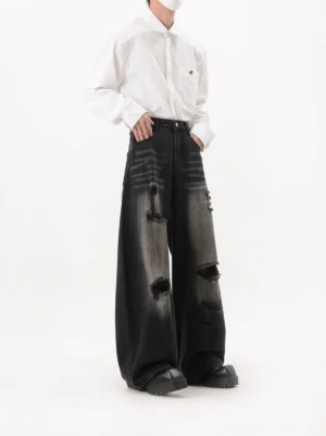 Side front view of black washed ripped wide leg jeans with whisker fading, loose streetwear fit, and distressed thigh panels
