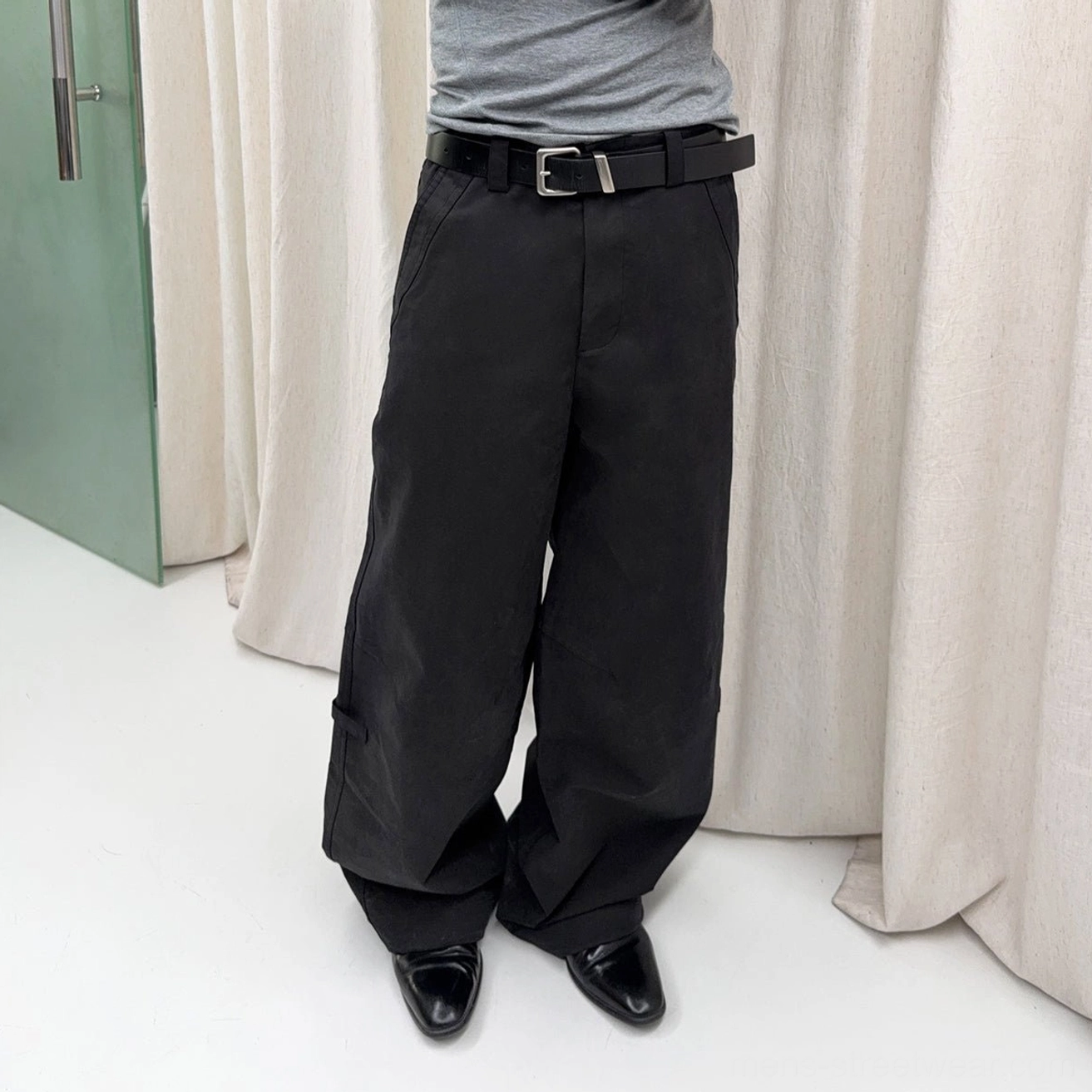 Black washed wide-leg cotton trousers shown in a cropped low-angle studio view with a relaxed streetwear fit, leather belt, and dress shoes