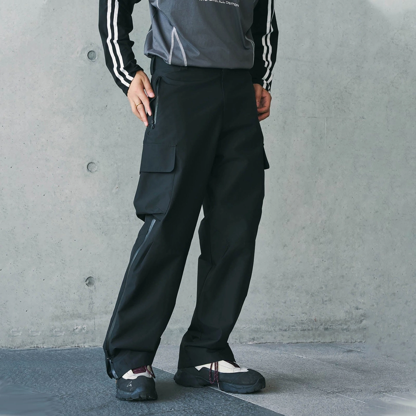 Black waterproof techwear cargo pants shown in a lower-body front view with large side pockets and ankle zippers