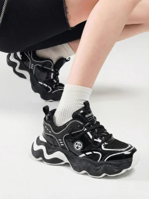 Black and white chunky dad sneaker worn with white socks and cropped black pants, showing the wavy sole, lace-up front, and layered upper