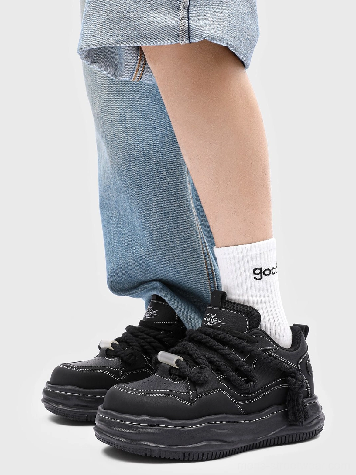 Black wavy platform sneaker worn with light blue jeans and crew socks, showing the distorted wave outsole in a casual everyday streetwear look
