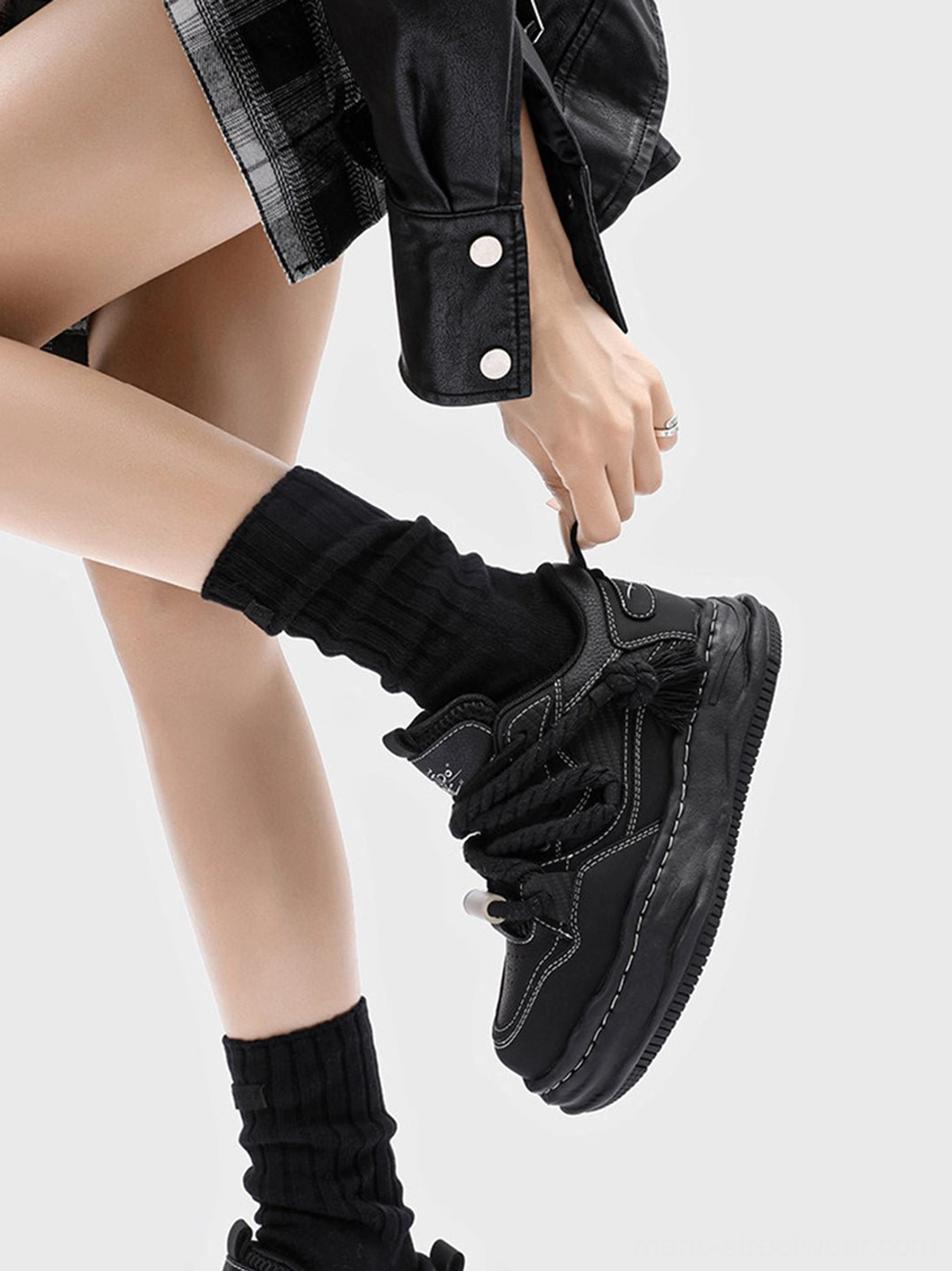 Back view of black wavy platform sneakers worn with black crew socks and a cropped leather jacket, highlighting the monochrome streetwear silhouette