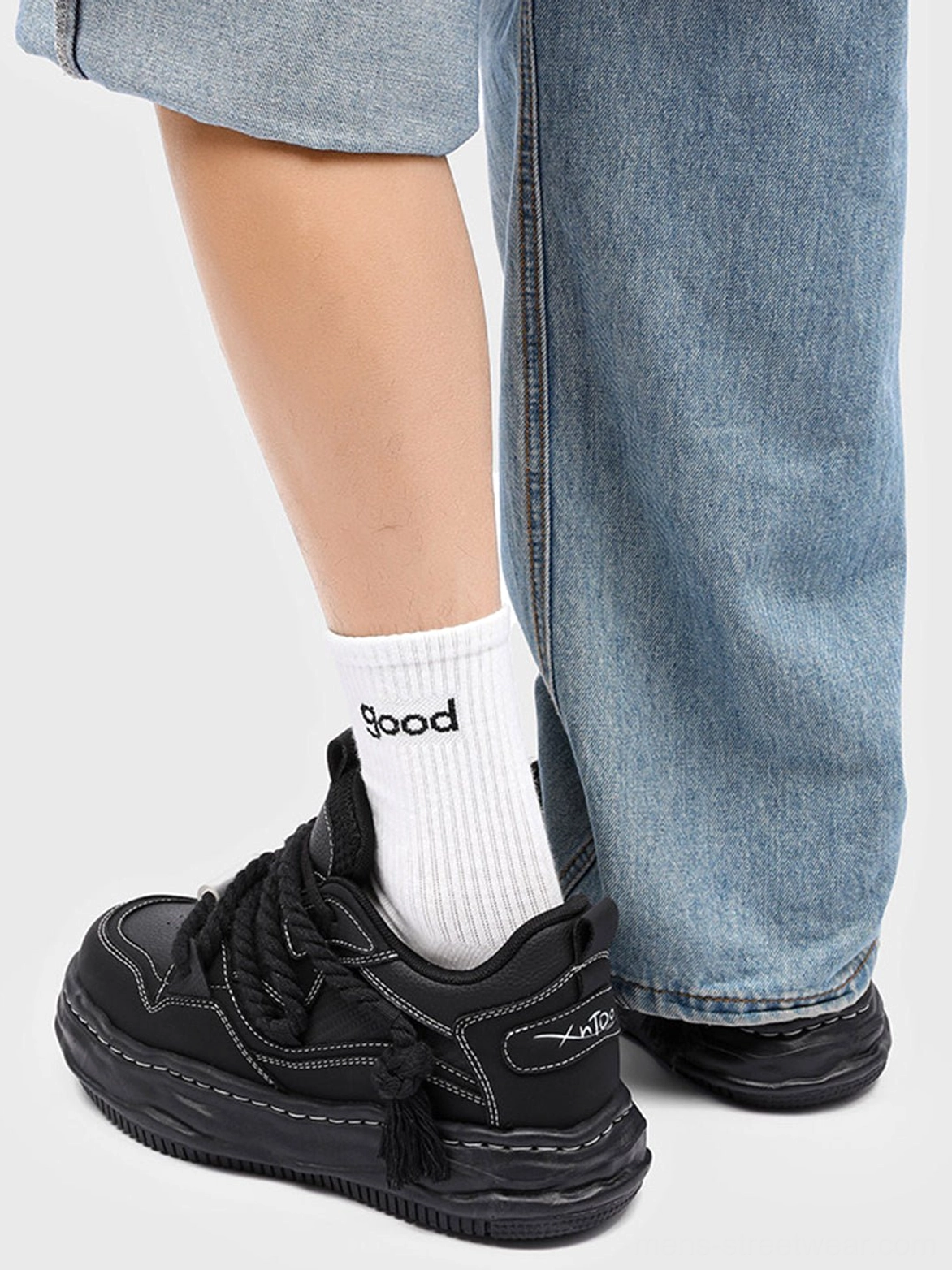 Side back view of black wavy platform sneakers styled with light blue denim and white crew socks, showing the heel logo detail and thick platform sole