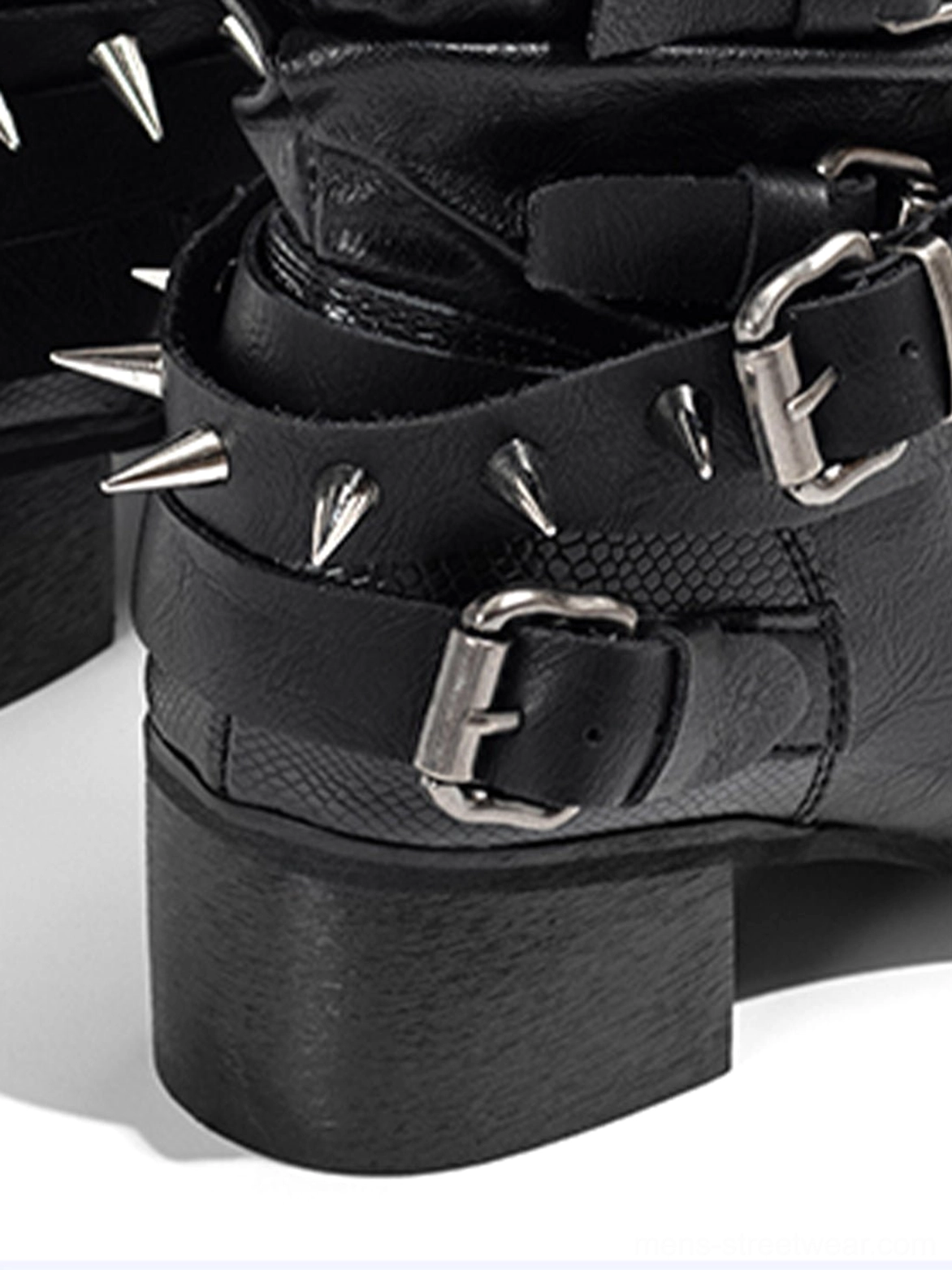 Close-up detail of black Western boots showing sharp metal spike studs, silver buckle fasteners, textured straps, and a chunky block heel