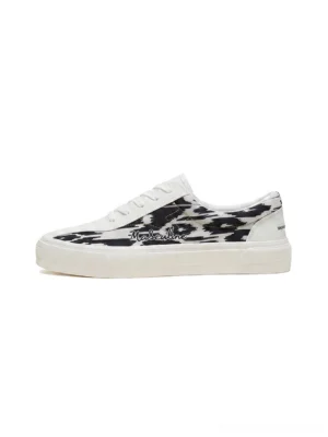 Side profile of black and white abstract cow print canvas skate shoes with white rubber outsole and low top streetwear silhouette