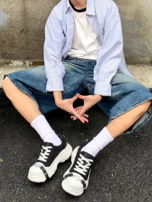 Male streetwear model wearing black and white buckle platform canvas sneakers with striped shirt, denim shorts, and white crew socks