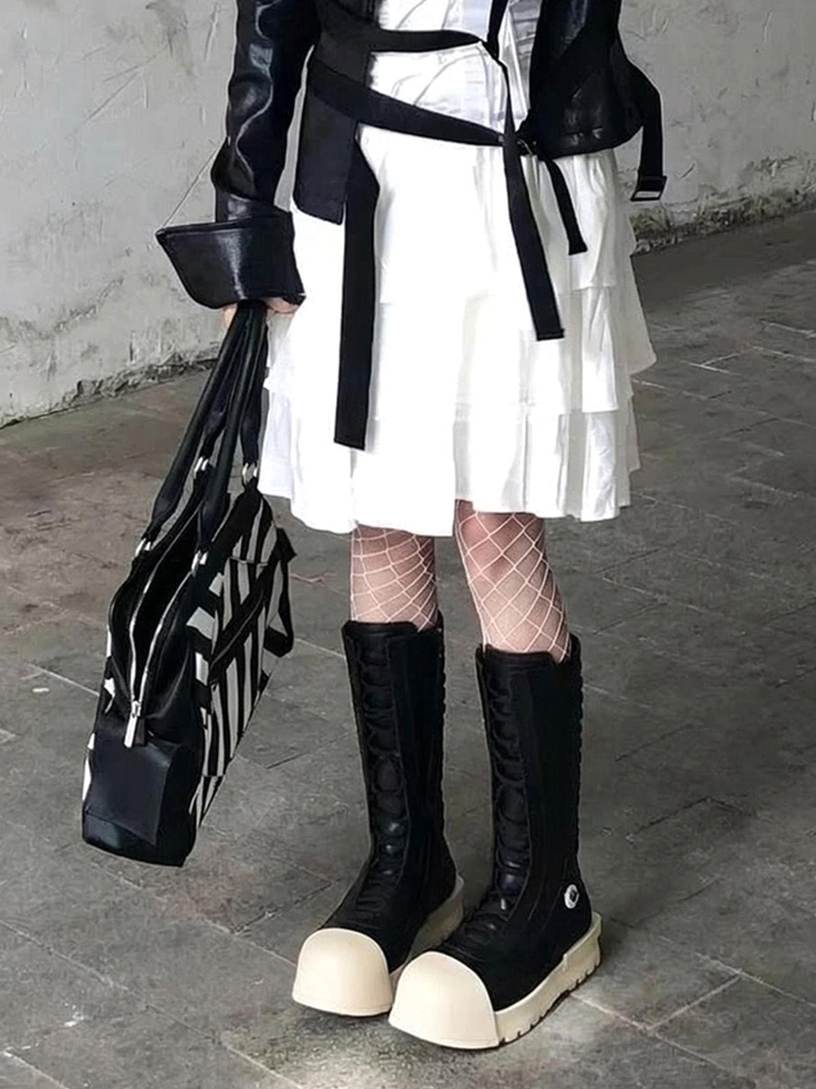 Black and white mid-calf platform boots styled with fishnet tights ruffled white dress and leather jacket in industrial fashion setting