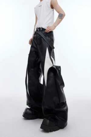 Black and white deconstructed faux leather wide-leg pants shown from a low-angle side view with oversized streetwear silhouette and detachable leather-effect drape