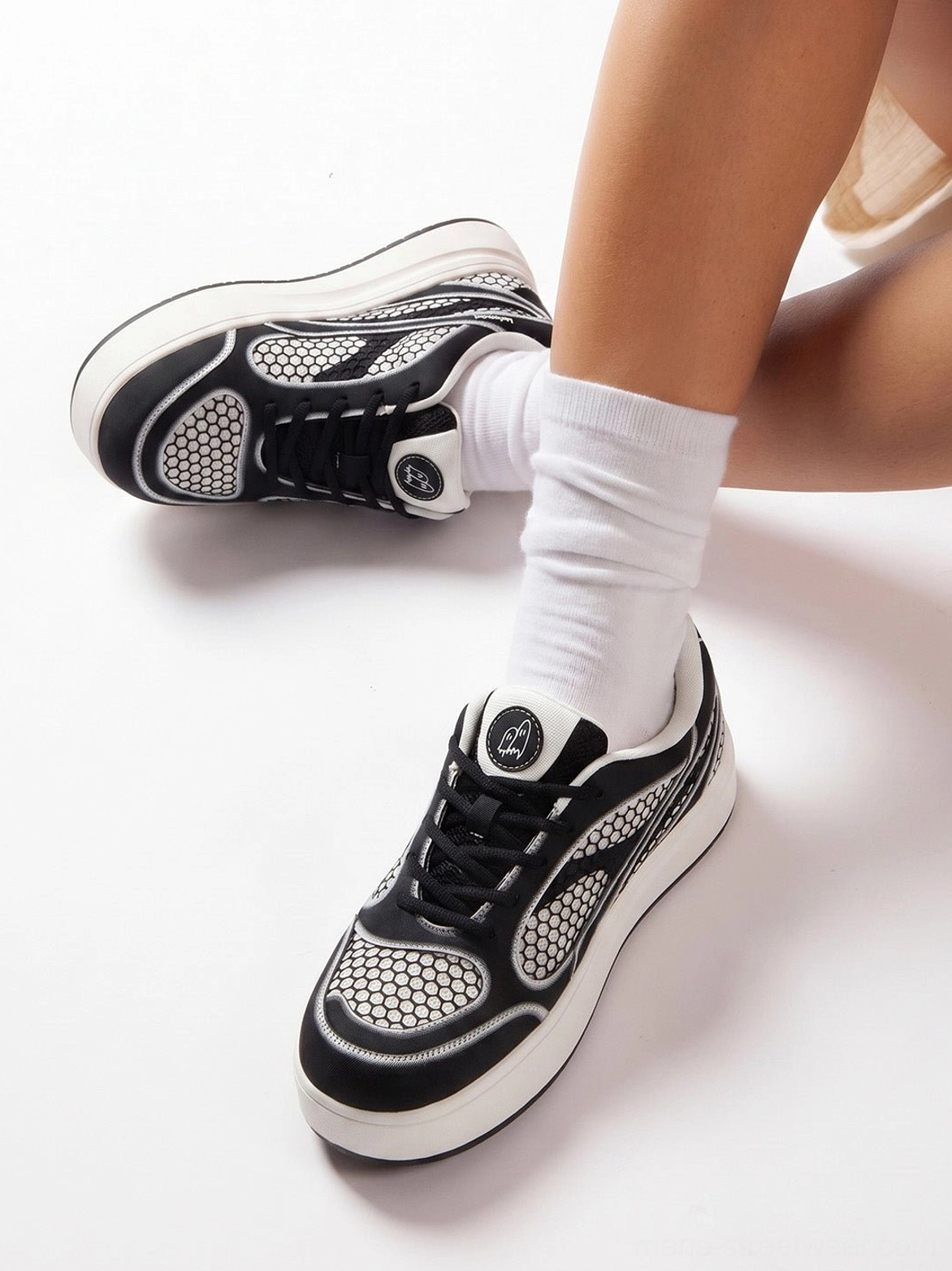 Top-down close-up of black and white mesh derby sneakers worn with white socks showing the lace-up upper and tongue logo