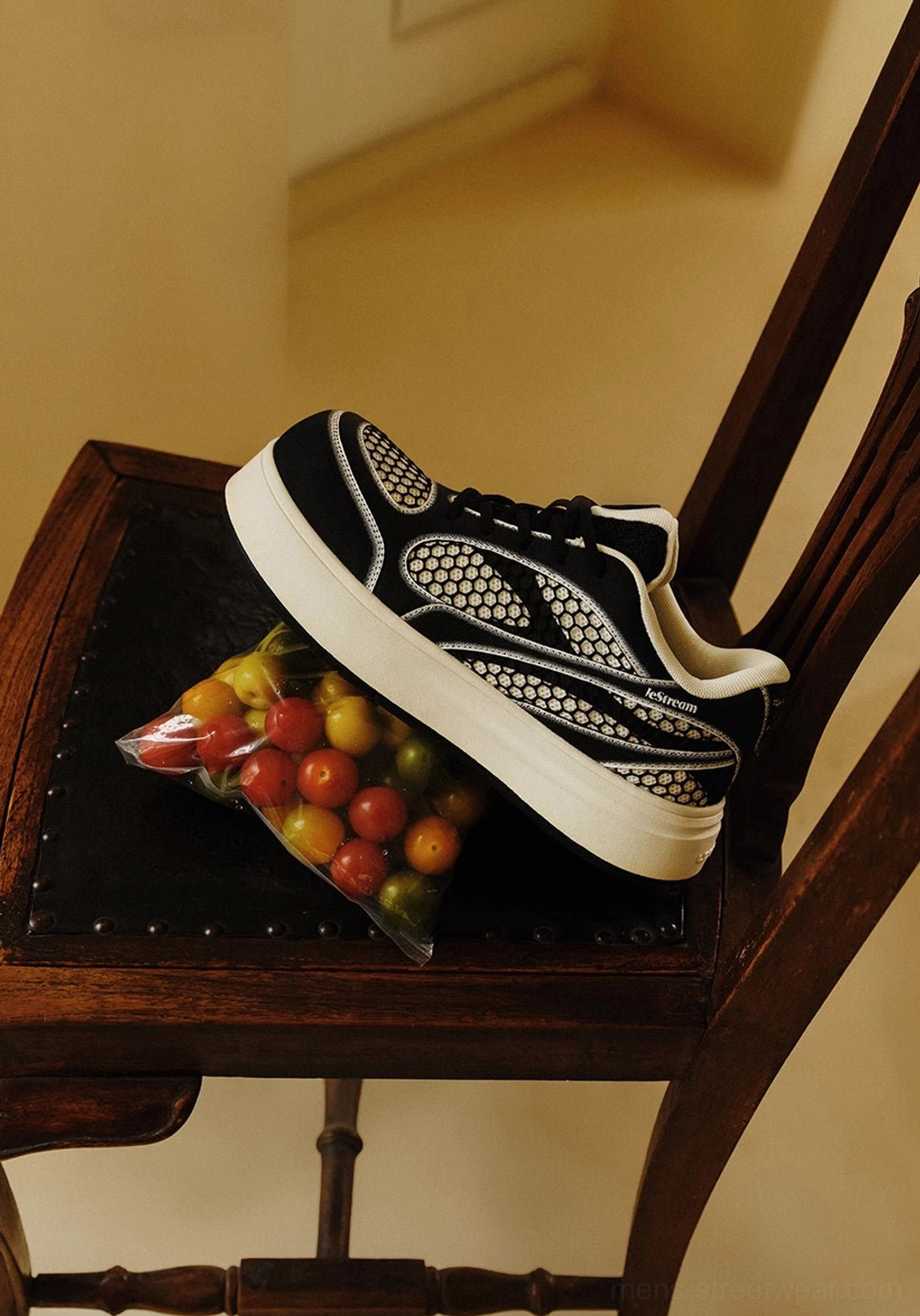 Three-quarter view of black and white mesh panel platform derby sneakers placed on a vintage wooden chair