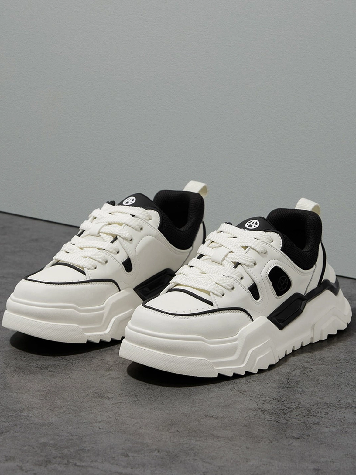 Pair of black and white monochromatic platform sneakers aligned front flat display on gray studio background showing contrast stitching details