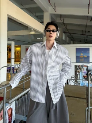 Black and white oversized vertical striped button-up shirt shown on male model in industrial streetwear shop