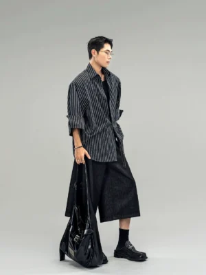 Relaxed black pinstripe button-down shirt worn open with rolled sleeves, black tote bag, socks, and loafers