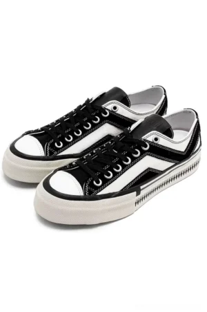 Black and white low-top platform canvas sneakers with black contrast toe caps and serrated rubber sole in angled front view