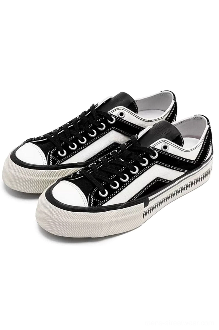 Black and white low-top platform canvas sneakers with black contrast toe caps and serrated rubber sole in angled front view