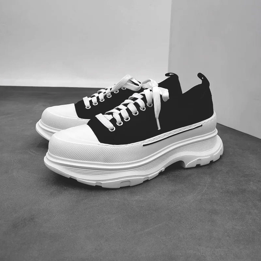 Pair of black and white platform canvas sneakers in a three-quarter flat lay with chunky white soles and loose laces