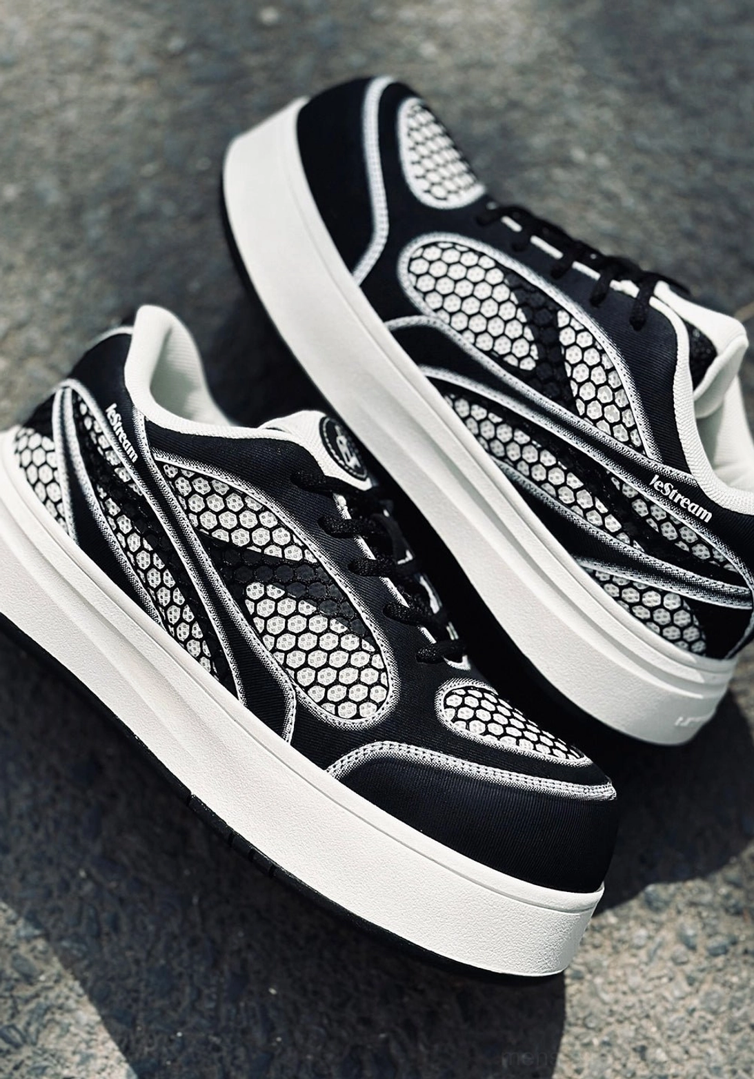 Overhead view of black and white platform derby sneakers displayed on an asphalt road with full mesh upper and white sole visible