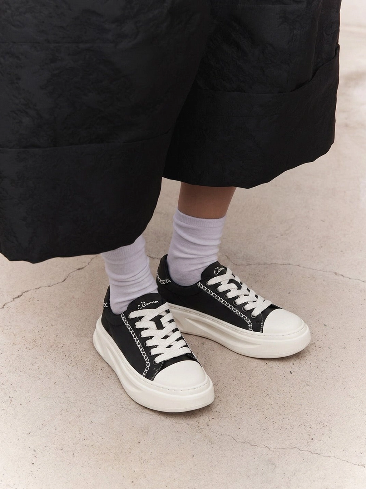 Black and white platform sneakers worn with white crew socks and wide-leg black culottes showing the chunky sole and low-top fit