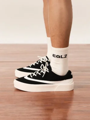 Black and white retro platform streetwear sneakers worn with white socks in a casual indoor outfit