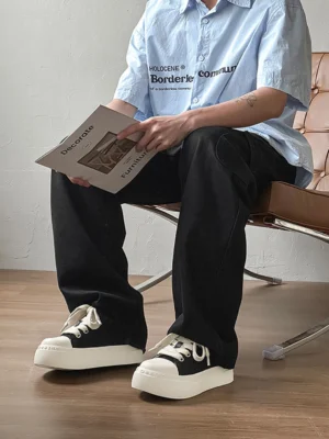 Male model wearing black and white platform streetwear sneakers with loose black wide-leg trousers in a casual outfit