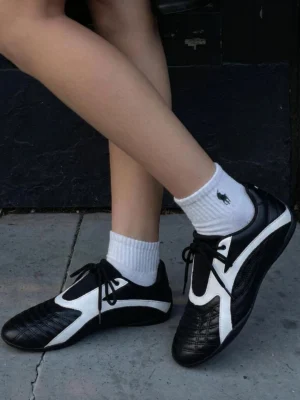 Black and white quilted flat sneakers worn with white crew socks in a low-angle streetwear outfit view on an outdoor concrete surface