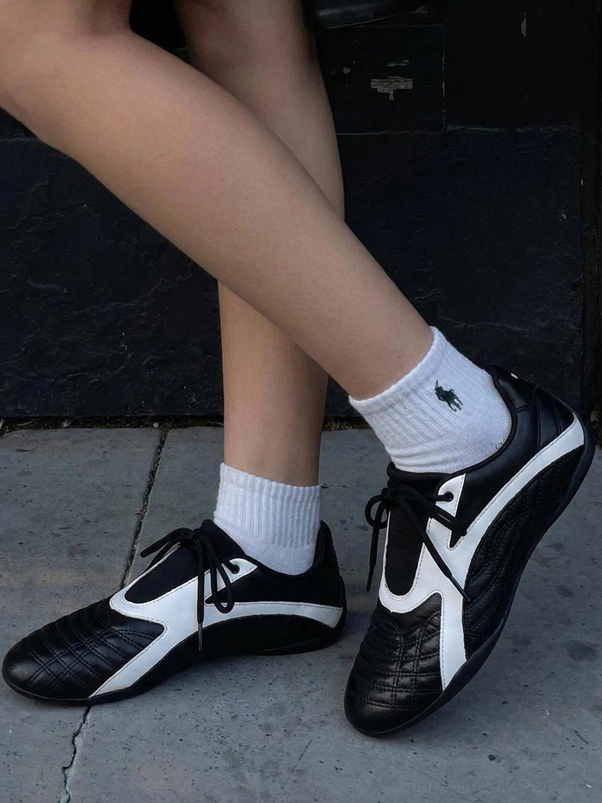 Black and white quilted flat sneakers worn with white crew socks in a low-angle streetwear outfit view on an outdoor concrete surface