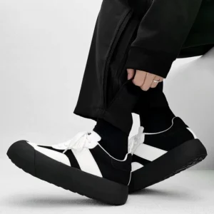 Black and white retro chunky sneakers worn with black cargo pants in a low side view, showing the thick platform rubber sole, layered panels, and lace-up streetwear design