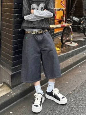 Black and white shell toe platform streetwear sneakers styled with white crew socks, cropped denim shorts, and layered urban clothing in a city alley