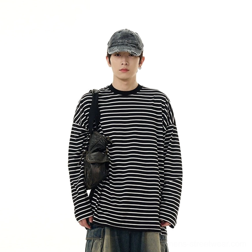 Full body front view of a relaxed black and white striped long sleeve streetwear tee with washed denim and leather crossbody bag