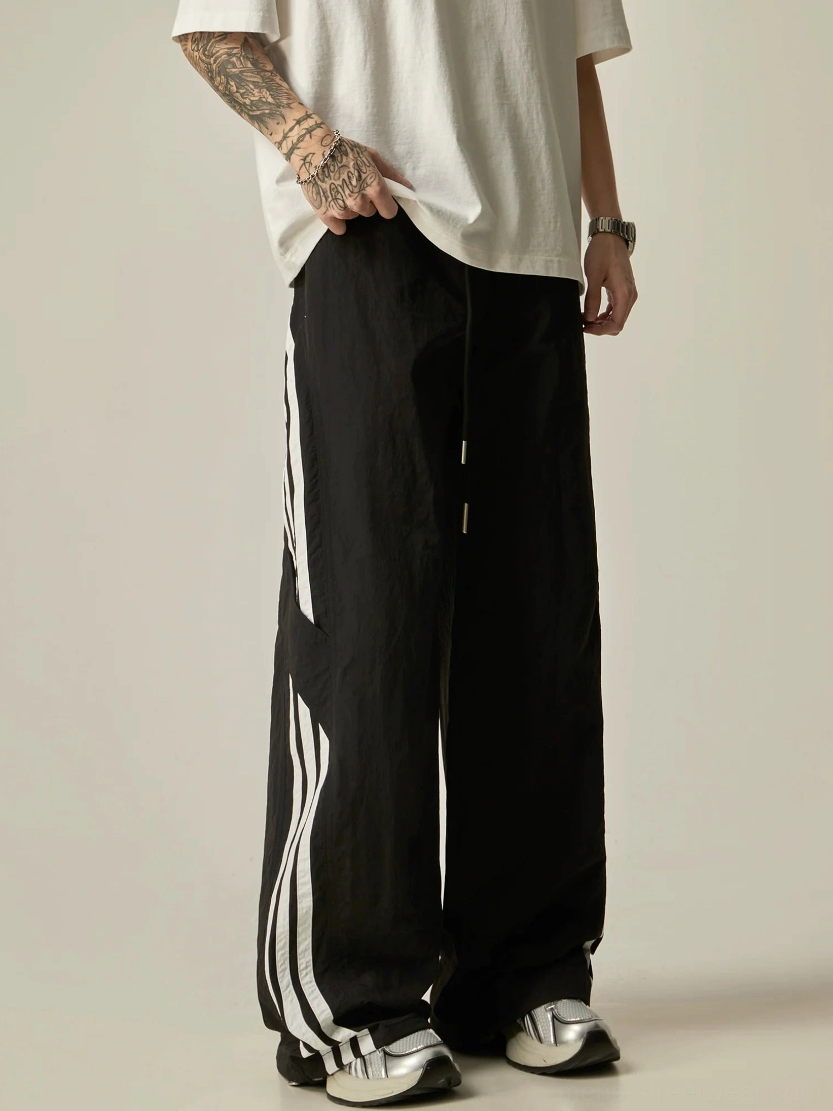 Side view of black wide-leg athletic track pants with contrasting white double side stripes, elastic drawstring waist, and relaxed streetwear fit