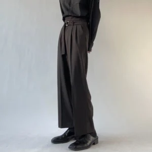 Black wide-leg belted trousers shown from the left side with a high waist, matching rectangular buckle belt, tailored drape, and black leather loafers
