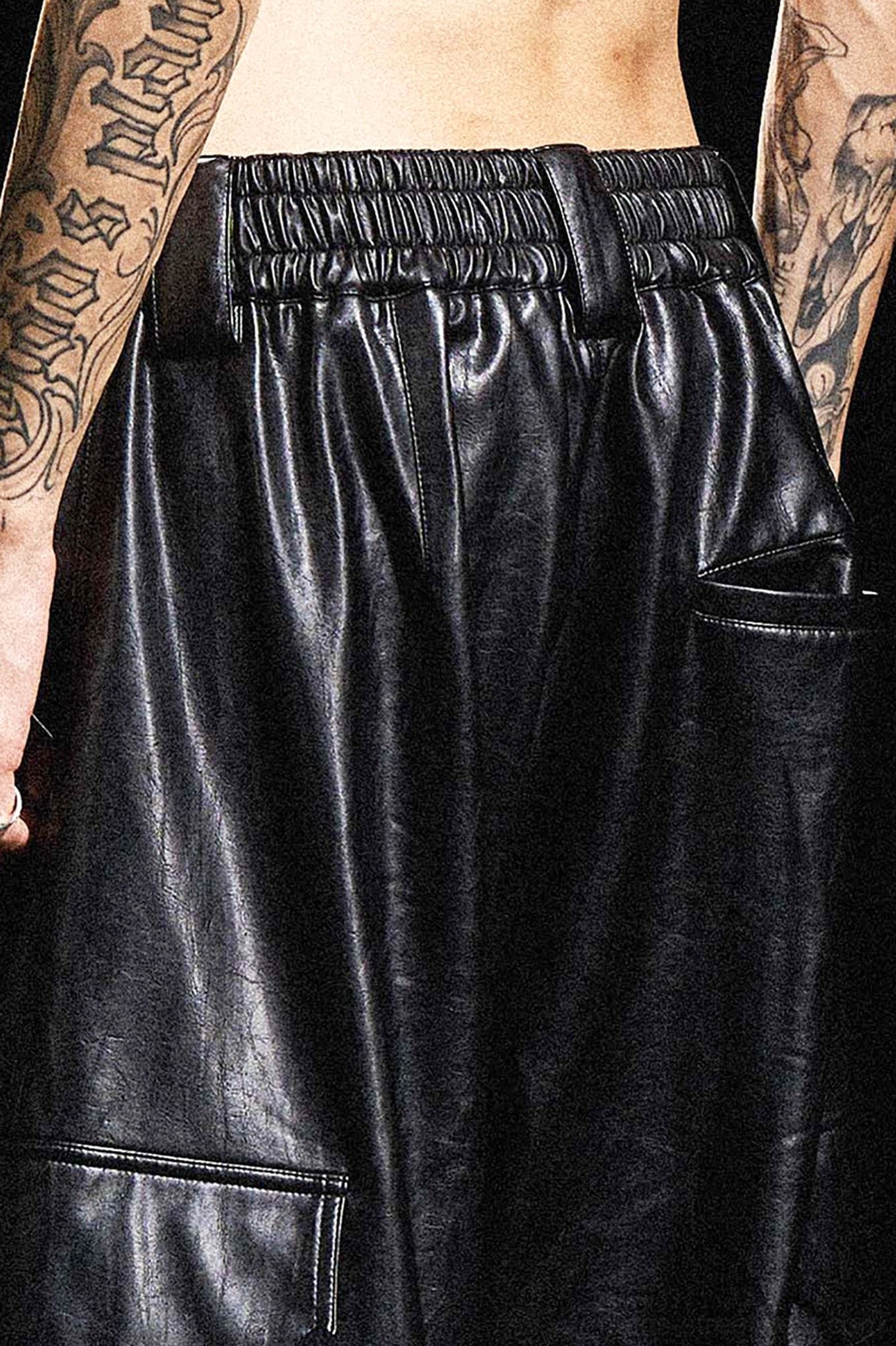 Front waist detail of black wide-leg cargo pants showing elasticated waistband, utility pockets and matte faux leather grain