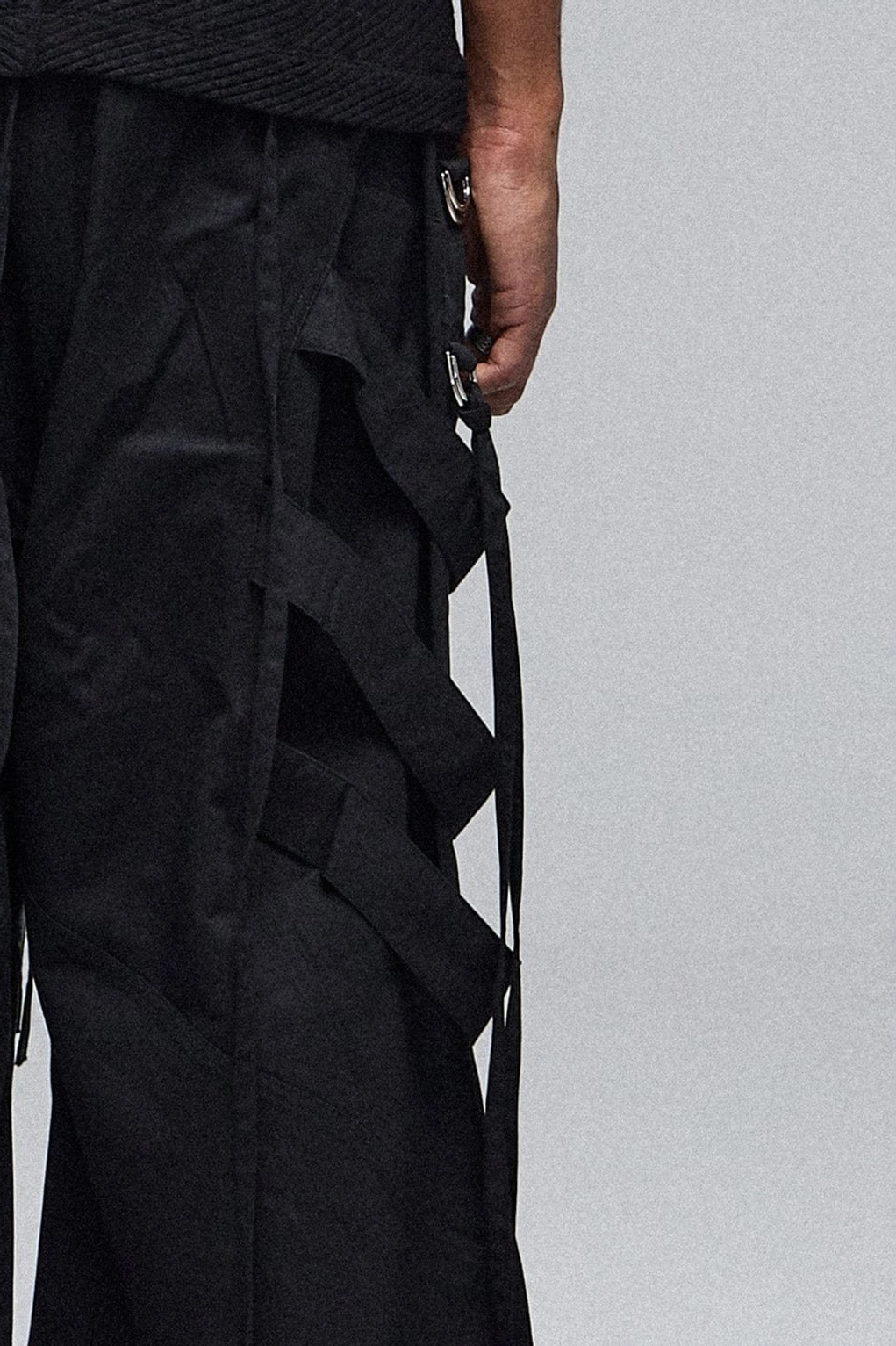 Side close-up of black wide-leg cargo pants with metallic strap details, zippered pocket accents, and relaxed utility streetwear construction