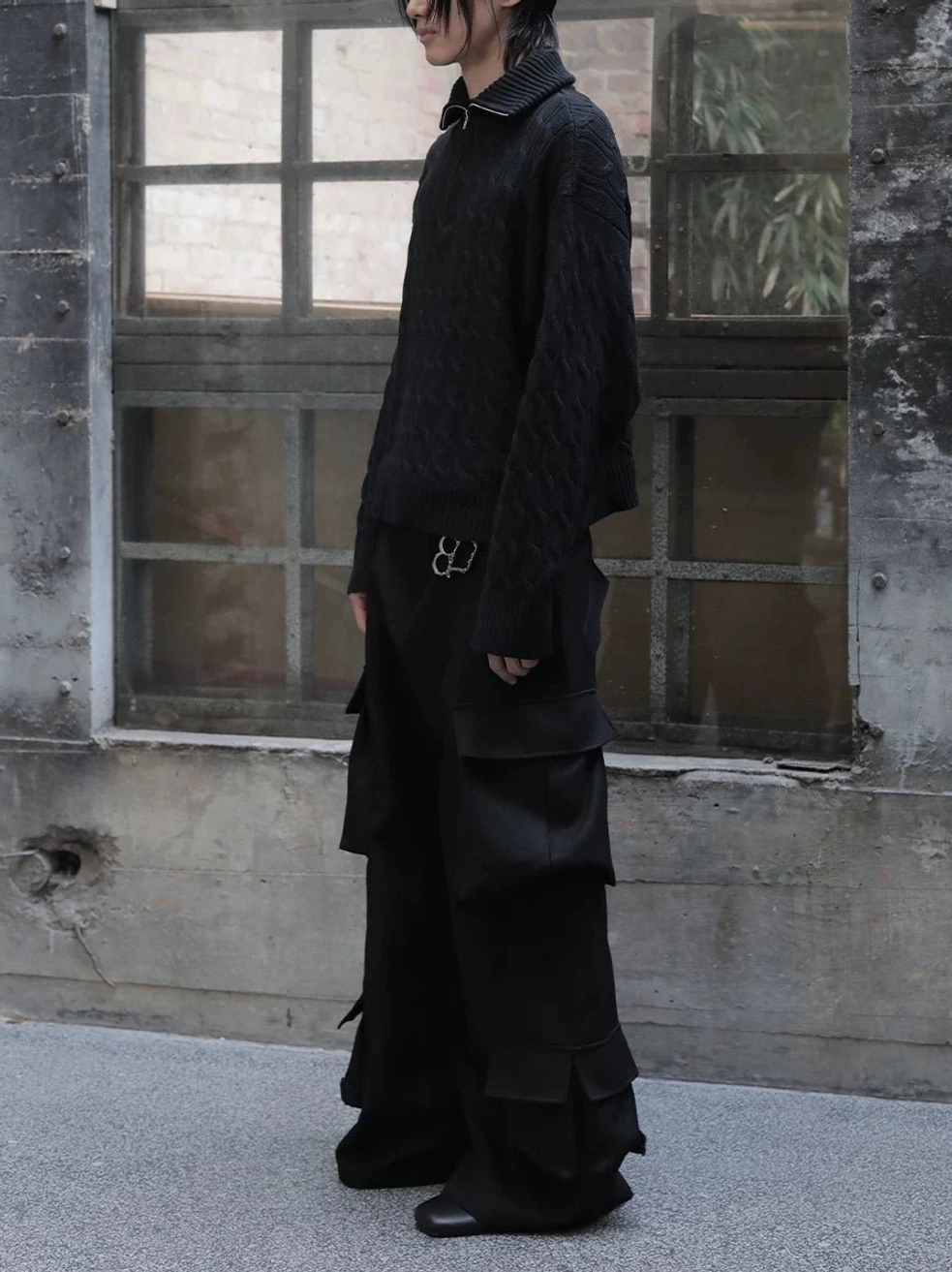 Black wide-leg cargo trousers styled with a black cable-knit sweater and waist chain in an industrial interior