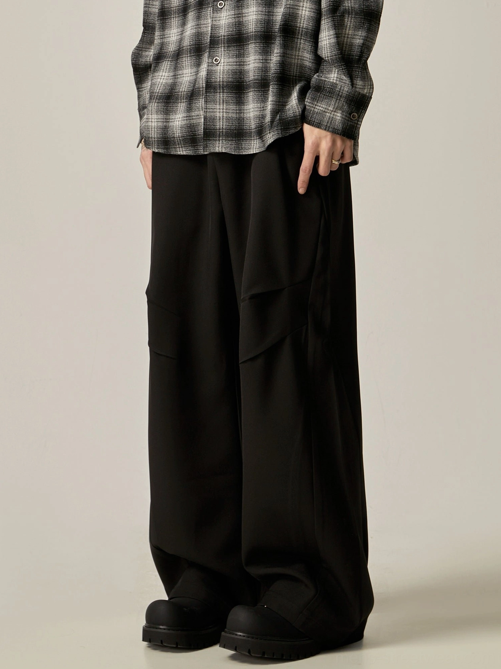Black wide-leg cargo trousers with relaxed draped fit, side pleated utility pockets, plaid shirt styling, and chunky black boots