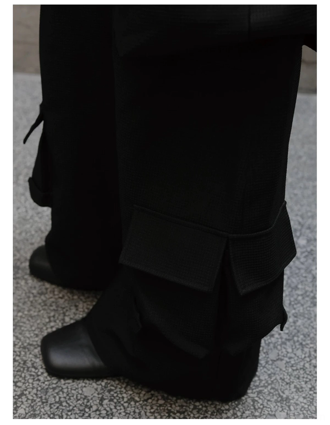 Close-up of wide black cargo trouser legs with lower-leg pockets and a clean tailored hem