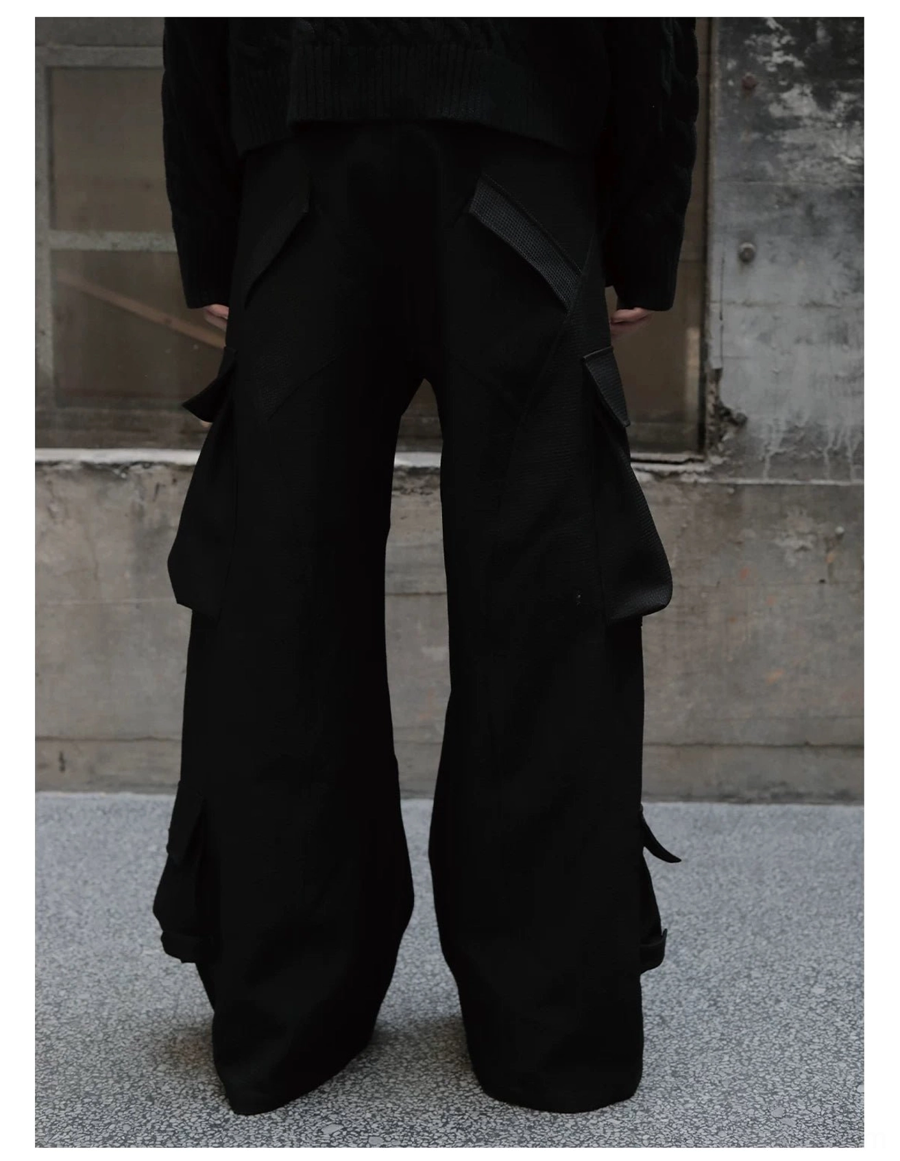 Rear full view of structured black wide-leg cargo trousers with utility pockets and a tailored hem