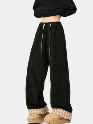 Front view of black wide-leg corduroy trousers with khaki plaid folded cuffs and drawstring waist styled with platform loafers
