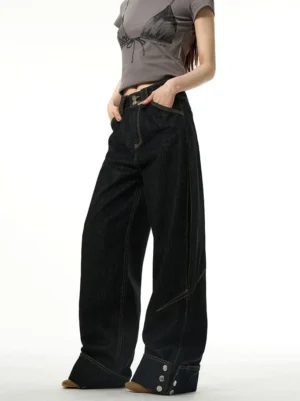 Black wide-leg cuffed jeans shown from a three-quarter front view with contrast yellow stitching, rolled hems, and metal button details styled with a cropped grey streetwear t-shirt