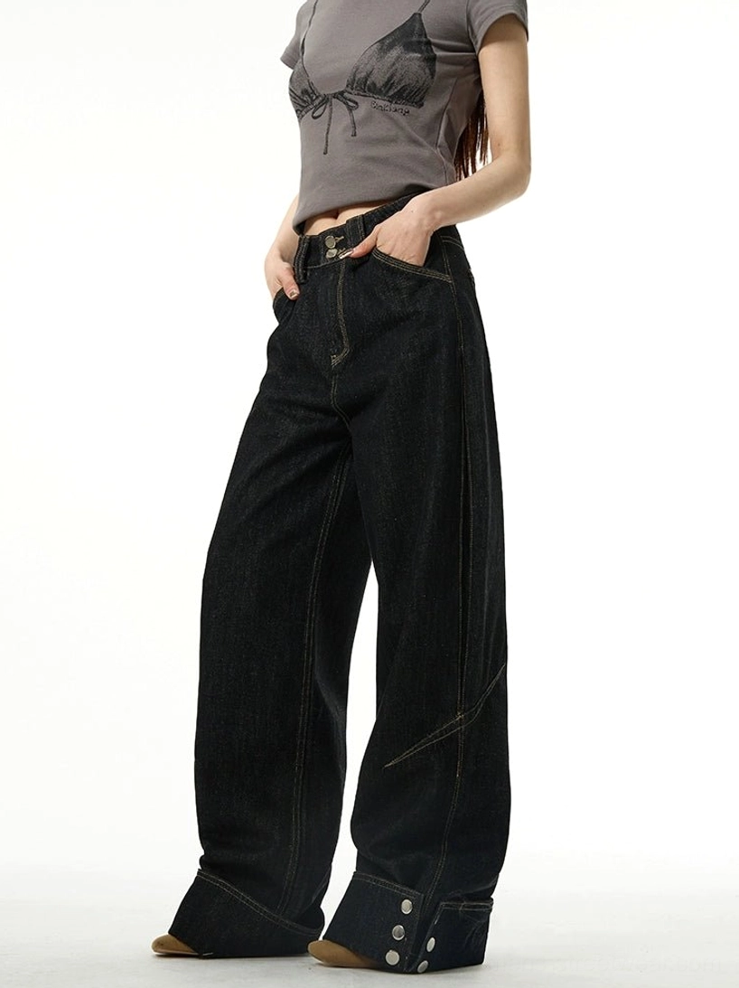 Black wide-leg cuffed jeans shown from a three-quarter front view with contrast yellow stitching, rolled hems, and metal button details styled with a cropped grey streetwear t-shirt