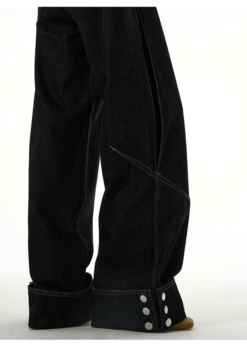 Side view of black wide-leg cuffed denim jeans showing diagonal leg seams, relaxed proportions, rolled hems, and metal button decoration