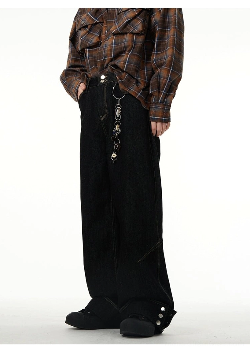 Three-quarter rear view of black rolled-cuff wide-leg jeans showing the metal waist pendant, back pockets, relaxed fit, and button-decorated hems