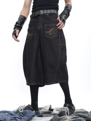 Front view of black wide-leg denim culotte shorts with curved panel seams and golden topstitching in an oversized streetwear fit