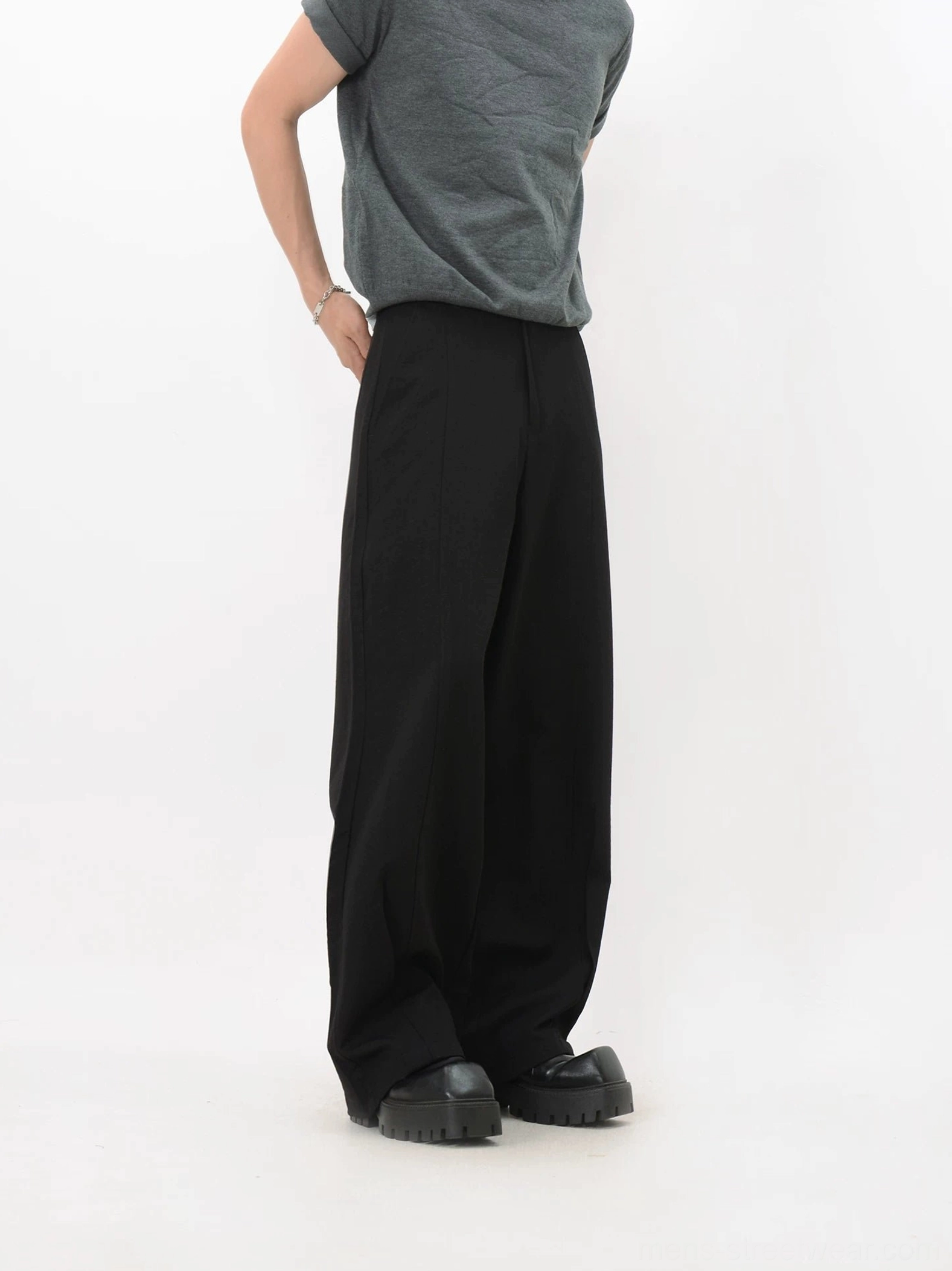 Three-quarter view of black wide-leg trousers showing the smooth draped fabric, relaxed tailoring, and full-length oversized fit