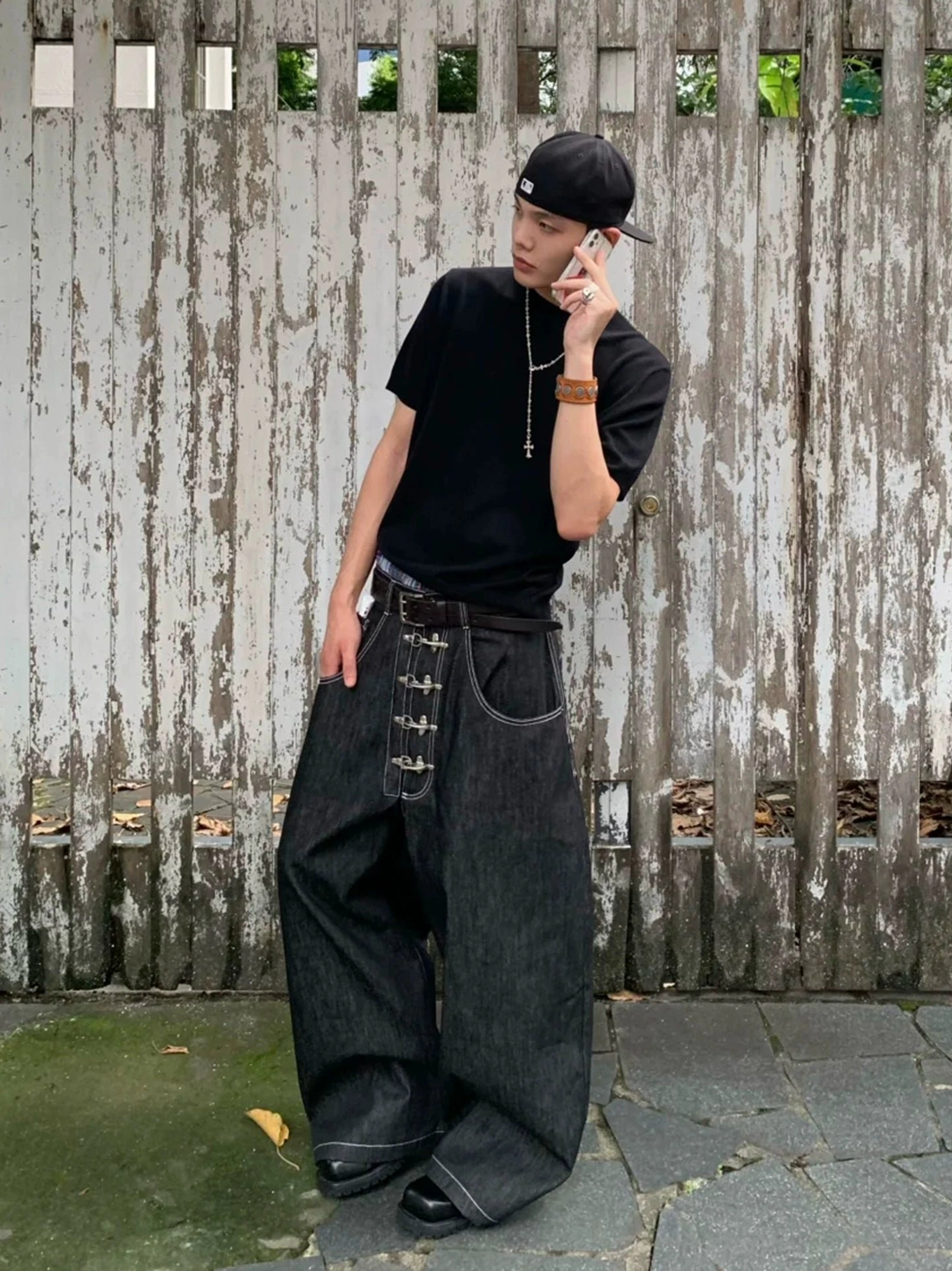 Side view of black wide leg hook closure contrast stitch jeans with black tee and baseball cap